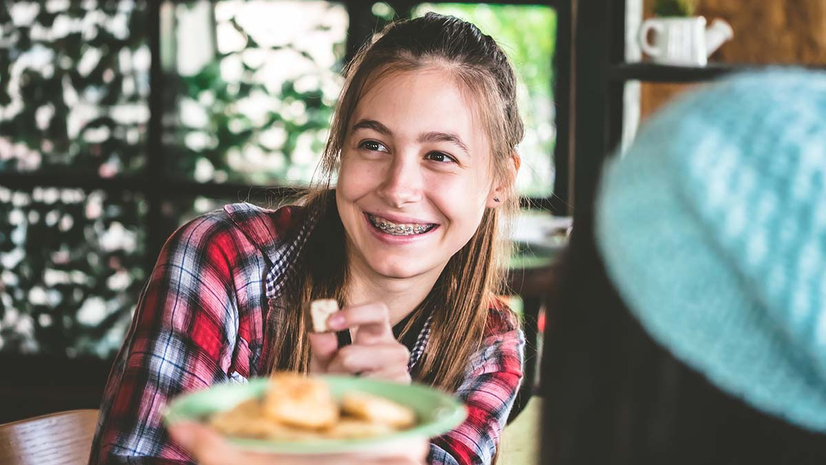 Young woman with braces confidently eating fruit, demonstrating a positive orthodontic experience.