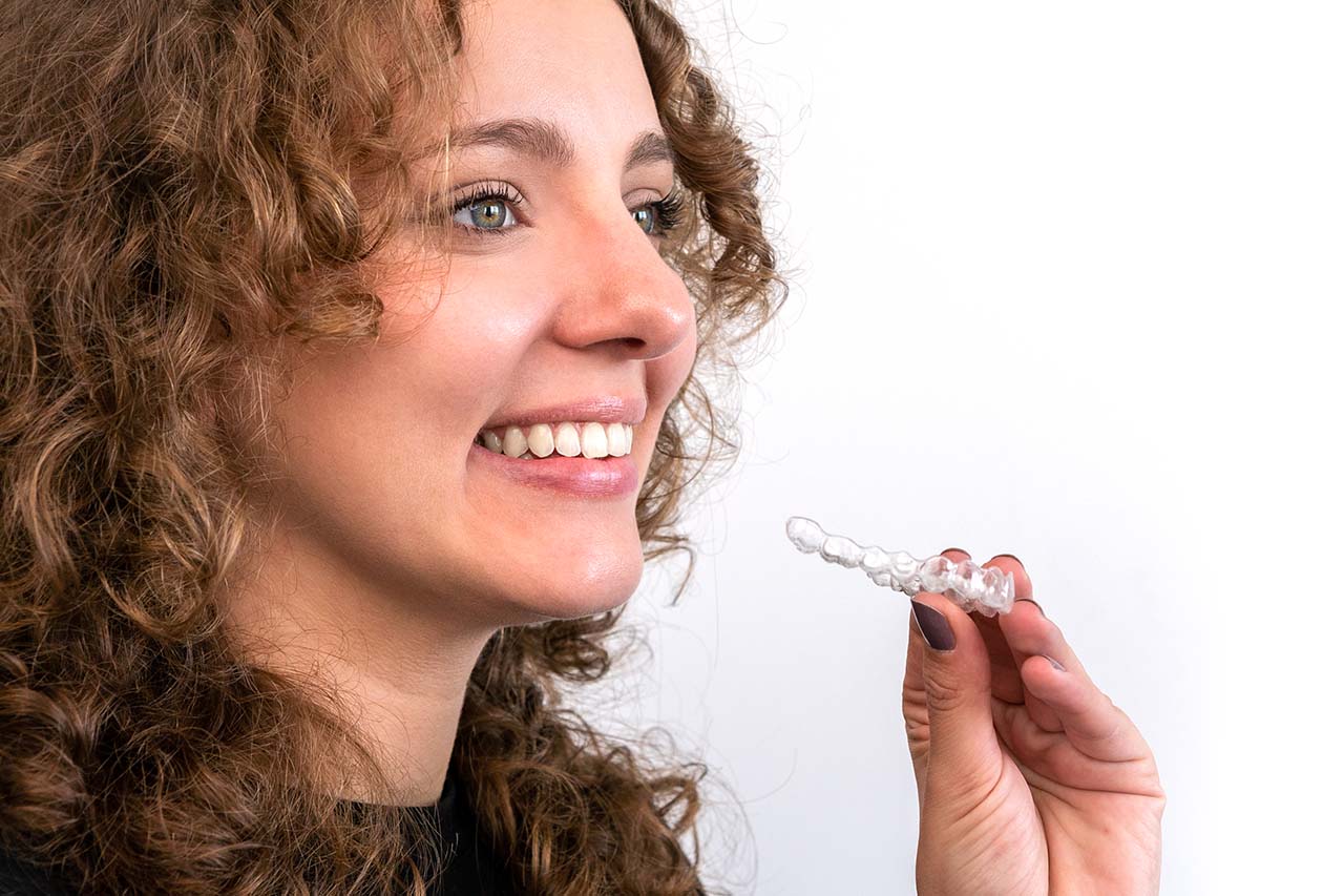 Woman smiling and holding a clear aligner tray, ready to insert SureSmile braces