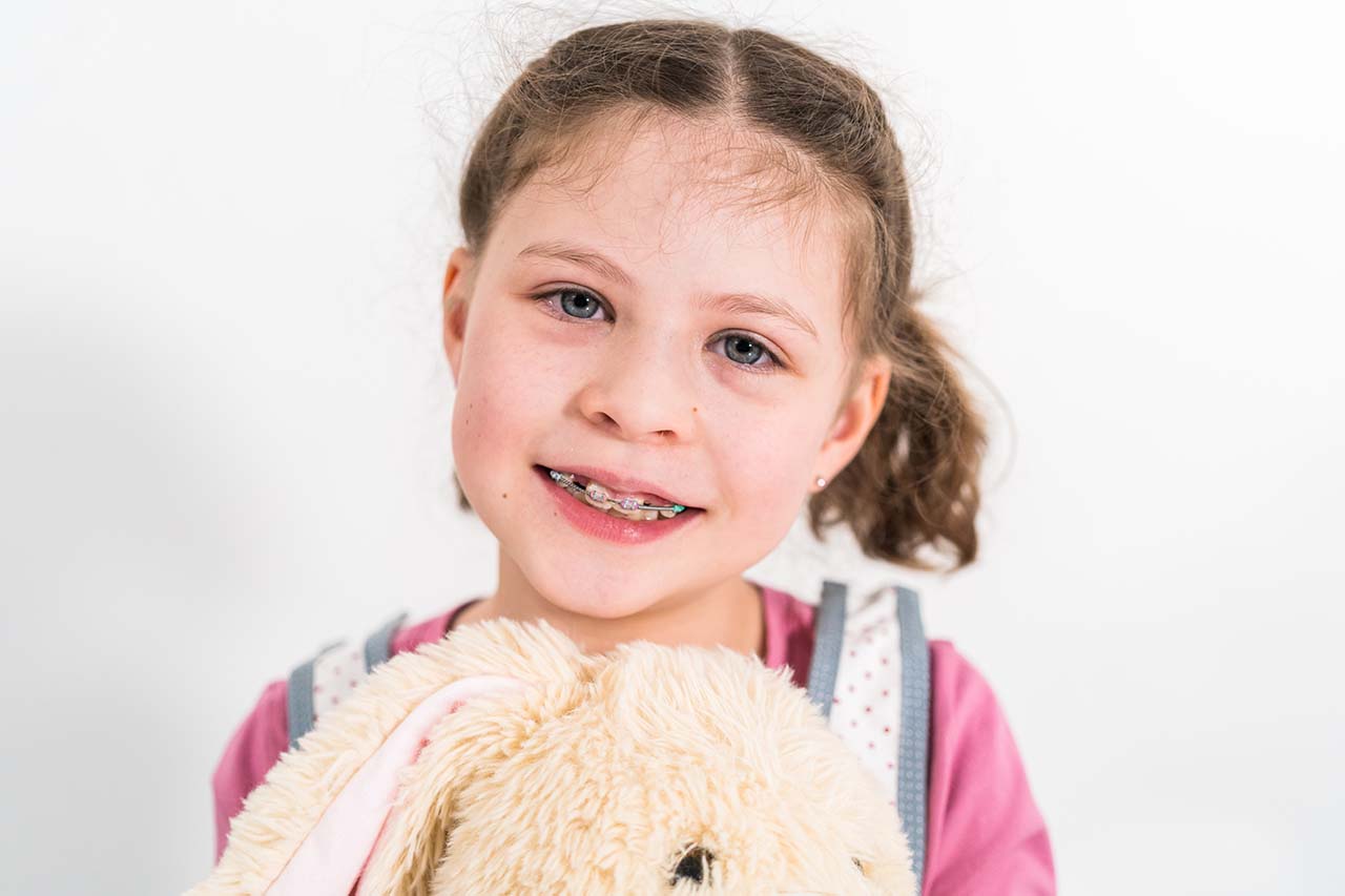 A joyful child with braces embraces a favorite toy, demonstrating the positive experience of wearing braces during early treatment.