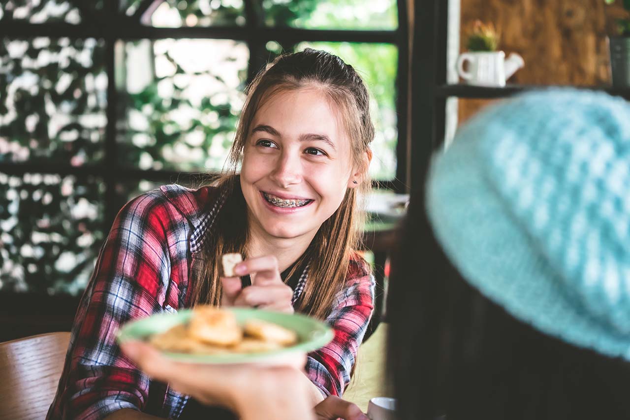 Teenage girl smiling with braces while eating a healthy snack at home.