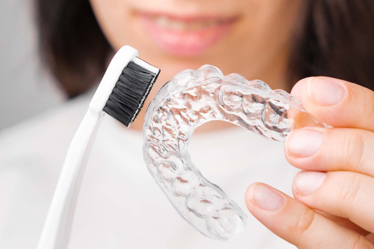 Woman brushing clear aligner with toothbrush, dental hygiene for braces, orthodontic care